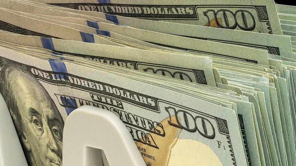 Billetes de dólar estadounidense apilados con cotizaciones en pantalla digital
