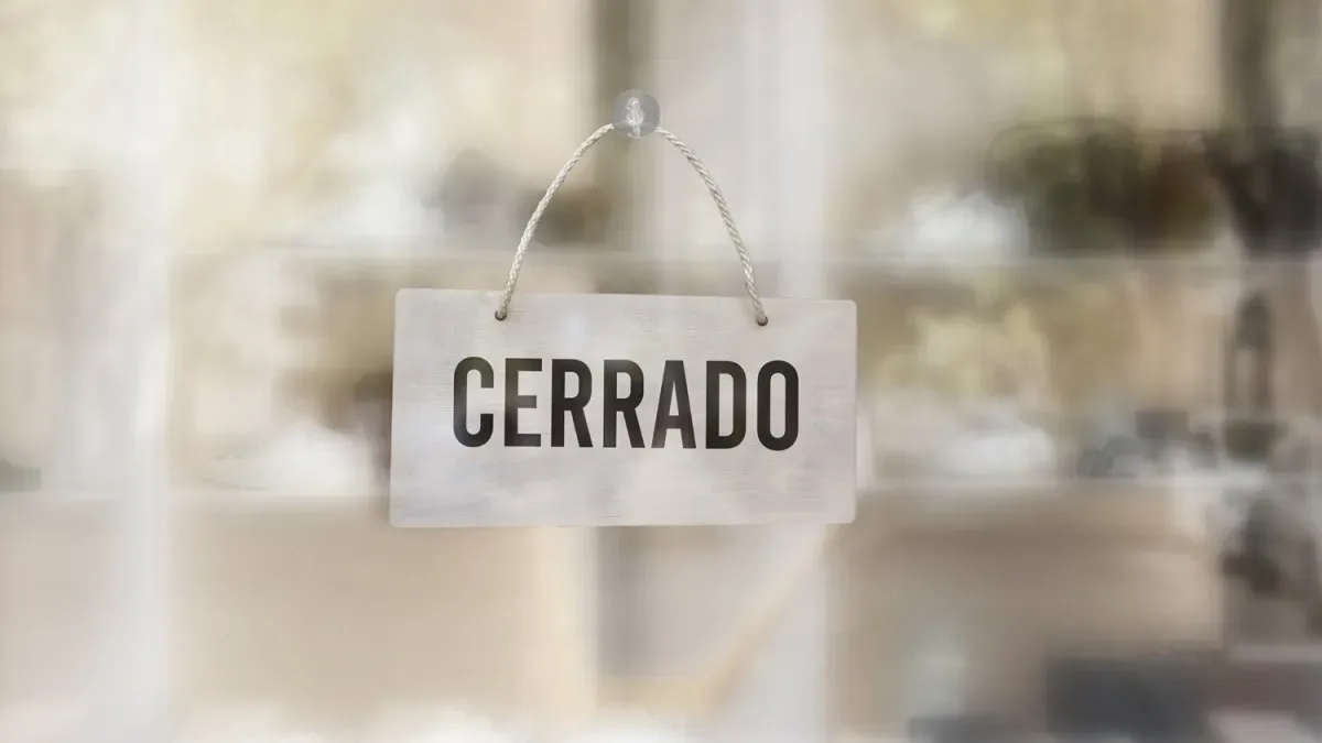 Fachada de supermercado grande con carteles de cierre definitivo y clientes saliendo