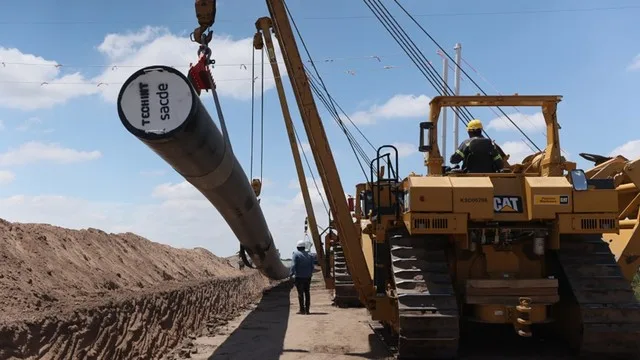 Tuberías de gasoducto en construcción en la estepa patagónica con equipamiento pesado al fondo