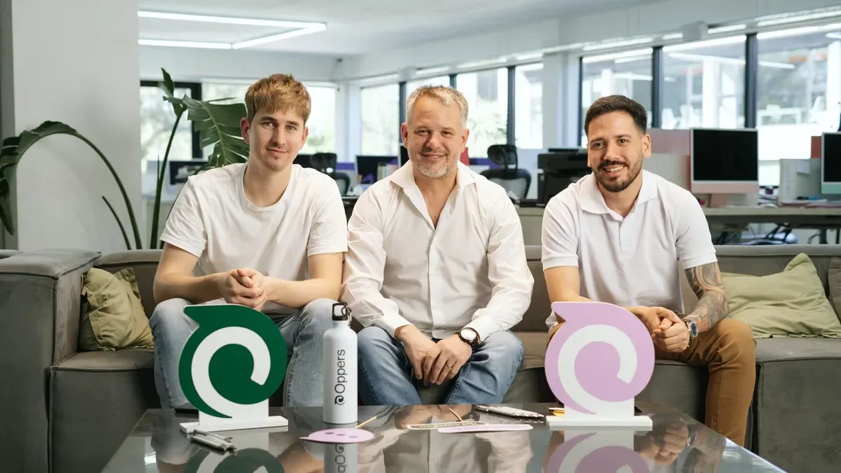 Tres jóvenes emprendedores trabajando en laptops en una oficina moderna con gráficos de encuestas en pantallas