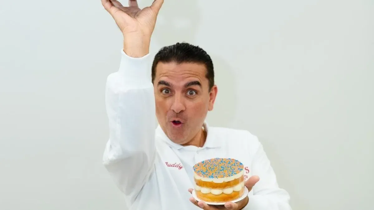 Buddy Valastro sonriente con un pastel elaborado en su pastelería Carlo's Bakery