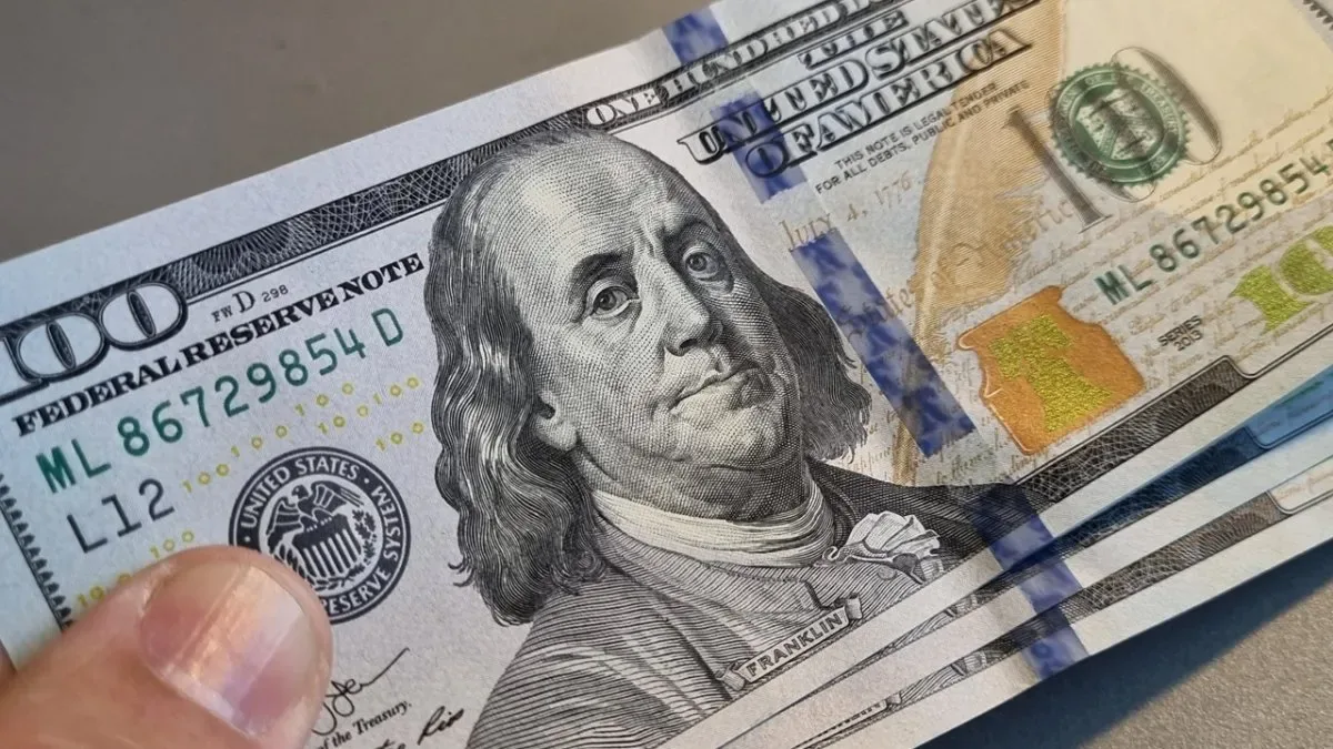 Billetes de dólar estadounidense apilados con cotizaciones digitales en pantalla
