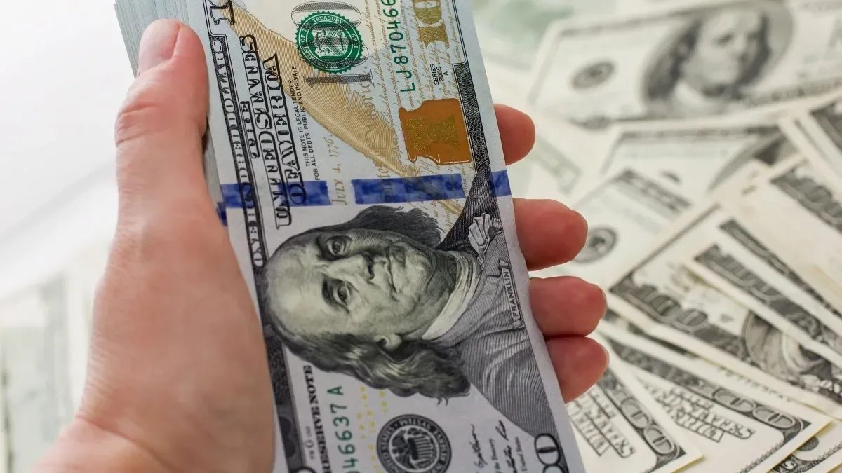 Billetes de dólares apilados y cotizaciones en pantallas de cambio