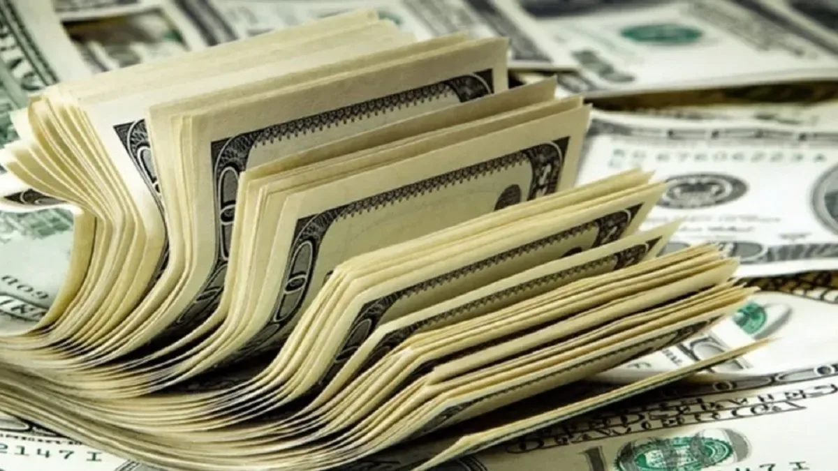 Billetes de dólares estadounidenses apilados con cotizaciones en pantalla digital