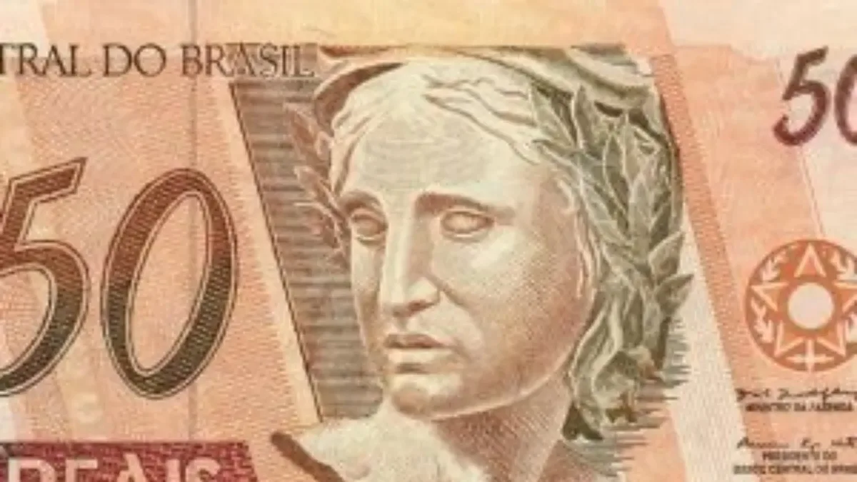 Billetes de reales brasileños y dólares sobre un escritorio con cotizaciones en pantalla