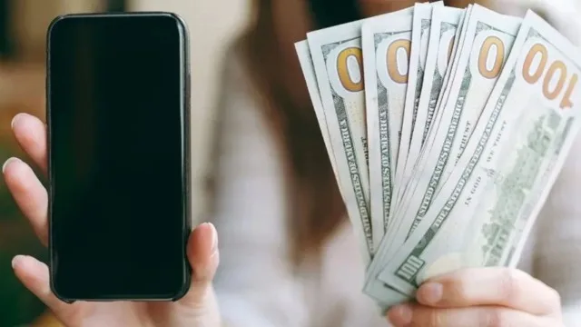 Mano sosteniendo un billete de 100 dólares bajo luz ultravioleta con app en smartphone
