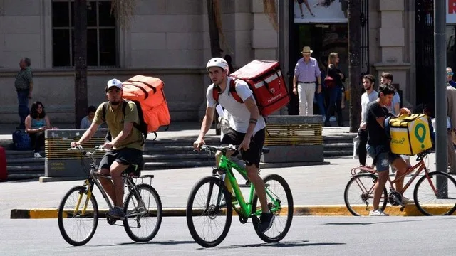 Repartidores en moto con celulares y apps de delivery en una ciudad argentina